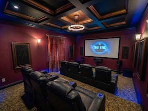 A home theater room with a large screen displaying 'THE END,' leather reclining chairs, a carpeted floor, and a ceiling with a circular light fixture.
