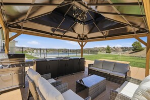 Un patio exterior con una parrilla, asientos y vistas a una piscina.