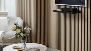 Una sala de estar moderna con una mesa de centro redonda, un televisor de pantalla plana montado en una pared de madera, y un jarrón con flores sobre la mesa.