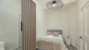 Un dormitorio con cama, mesitas de noche, una lámpara colgante y un separador de madera.