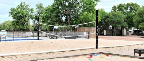Un terrain de volleyball de sable avec un filet, entouré d’arbres et d’une clôture.