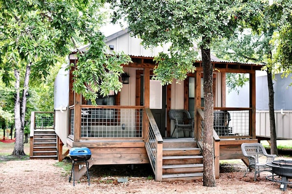 Una cabaña de madera con porche, una parrilla y una silla.