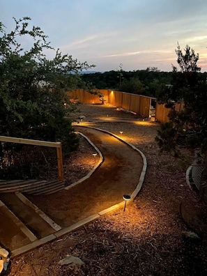 Een aangelegde tuin met een kronkelend pad, houten constructies en sfeerverlichting.