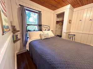 Ein Schlafzimmer mit Bett, einem Fenster mit Vorhängen, einem Nachttisch und einem Kleiderschrank.