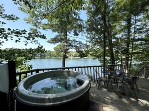 Un bain à remous sur une terrasse en bois, avec vue sur un lac et des arbres.