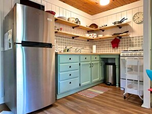 Eine Küche mit einem Edelstahl-Kühlschrank, hellblauen Schränken, Holzregalen, einer Uhr und einem weißen Herd.