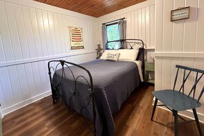 Ein Schlafzimmer mit Bett, Sessel, einem Fenster mit Vorhängen, einem Wandzeichen und einer Wanddekoration.