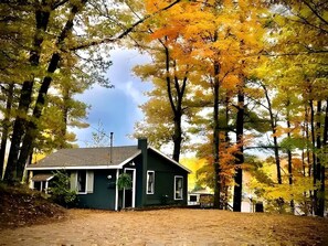 Une maison de plain-pied à l’extérieur sombre, entourée d’arbres aux feuilles d’automne.