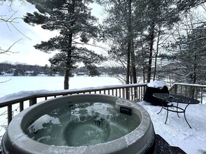 Un bain à remous sur une terrasse enneigée, avec vue sur un lac et des arbres.