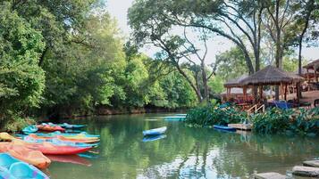 A calm river with colorful boats, a thatched-roof structure, and lush greenery.