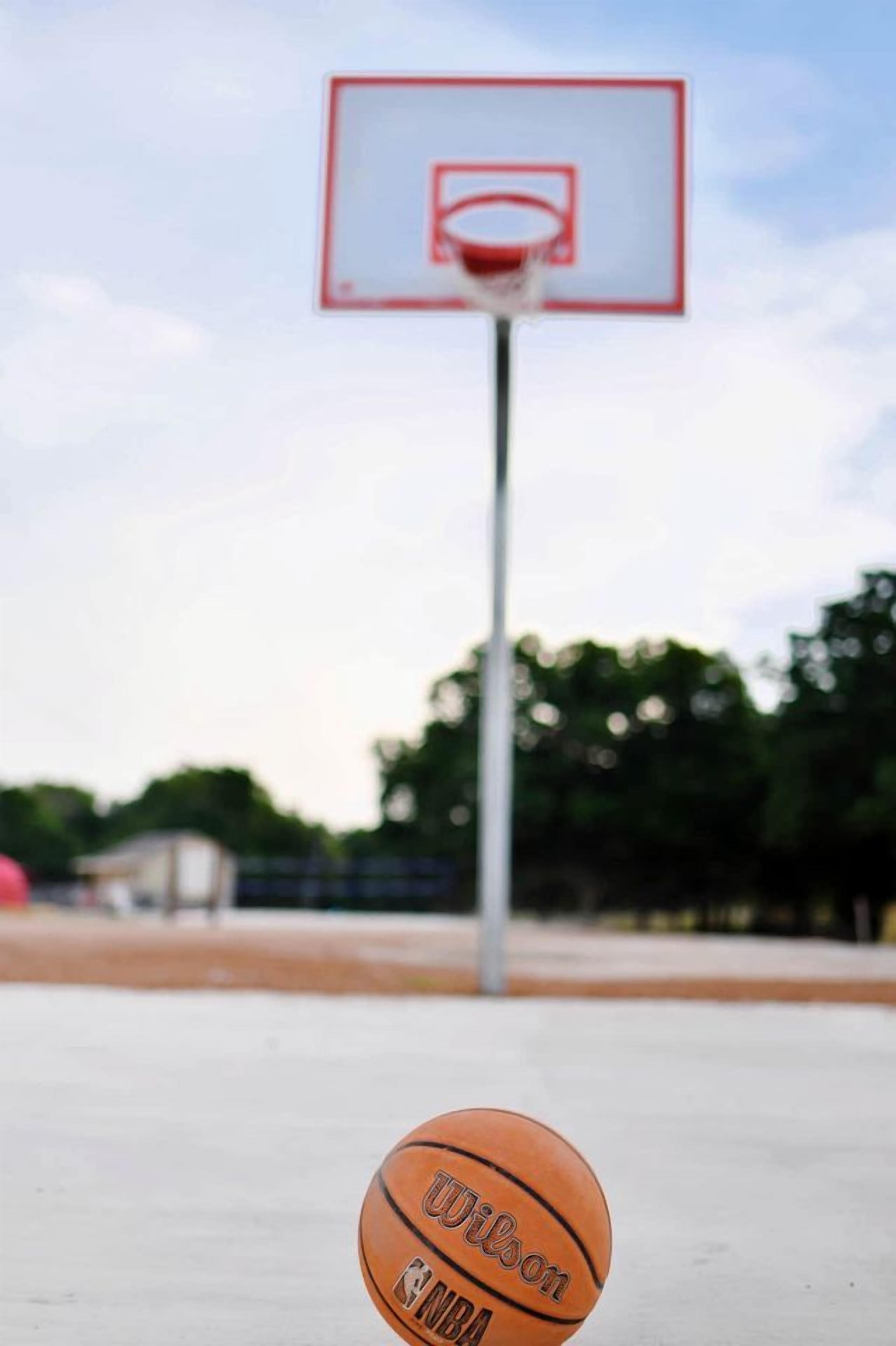 Una canasta de baloncesto con red, un balón de baloncesto y un cielo despejado.