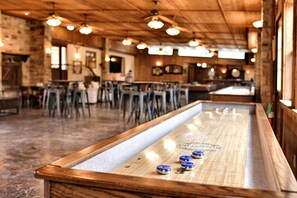 A bar area with a shuffleboard table, wooden ceiling, and bar stools. - Safari Tent Tranquility in the Heart of Texas, Perfect for Glamping in Cibolo (Cibolo)