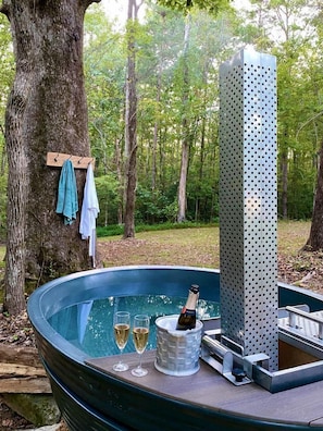 A hot tub with two glasses of champagne, a bottle, and a metal structure in a forested area.