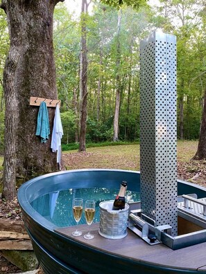 Un jacuzzi con dos copas de champán, una botella y una estructura metálica en un área boscosa.