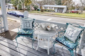 Eine Veranda mit zwei Stühlen und einem kleinen Tisch, jeweils mit einem Kissen, auf dem steht: 'Komm und setz dich auf die Veranda mit mir'.