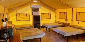 A tent with three beds, a coffee maker, and a small table.