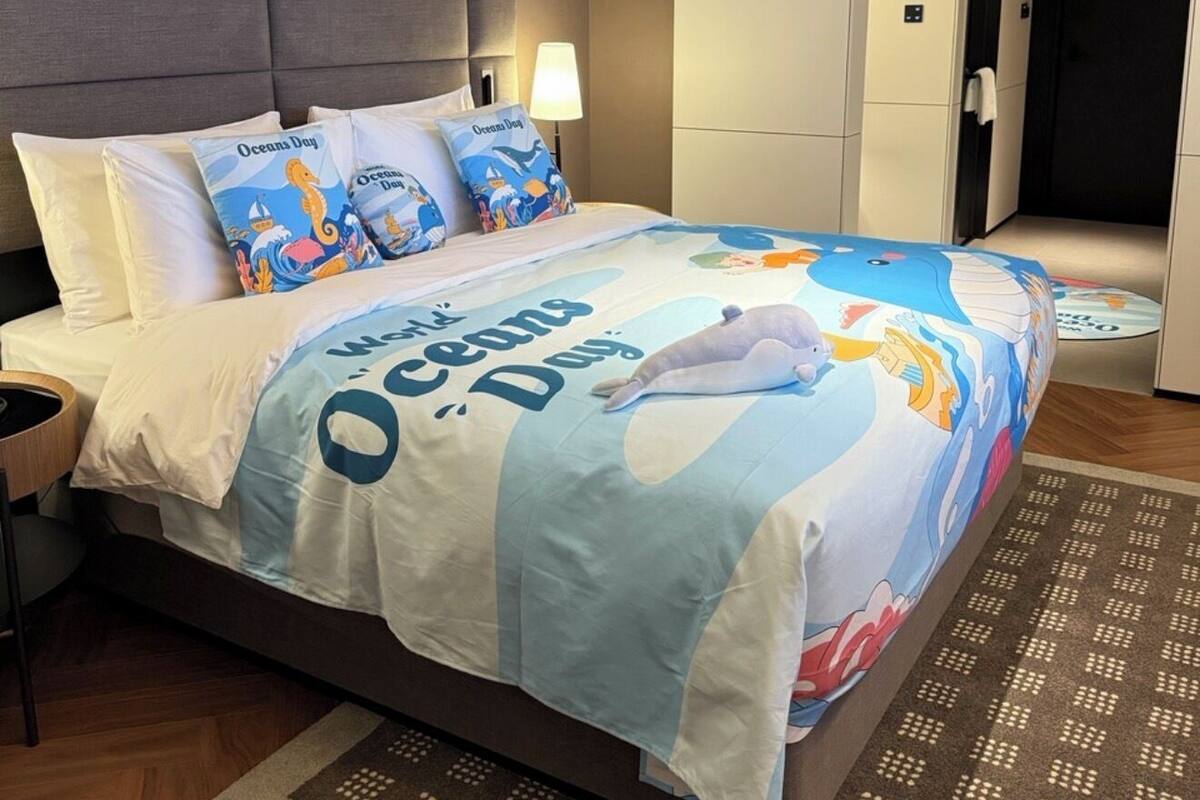 A hotel room with a bed featuring a themed bedspread, a bedside lamp, and a headboard.