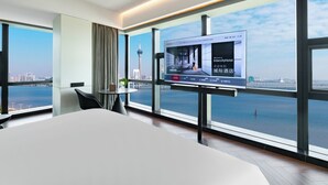 Habitación de hotel moderna con una cama grande, un televisor en la pared y vistas a un horizonte urbano y al agua.