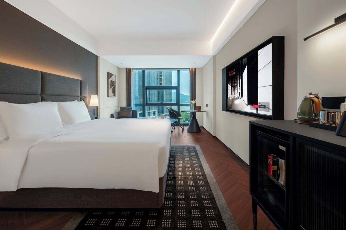 A hotel room with a large bed, a desk, a television, and a view of the city.