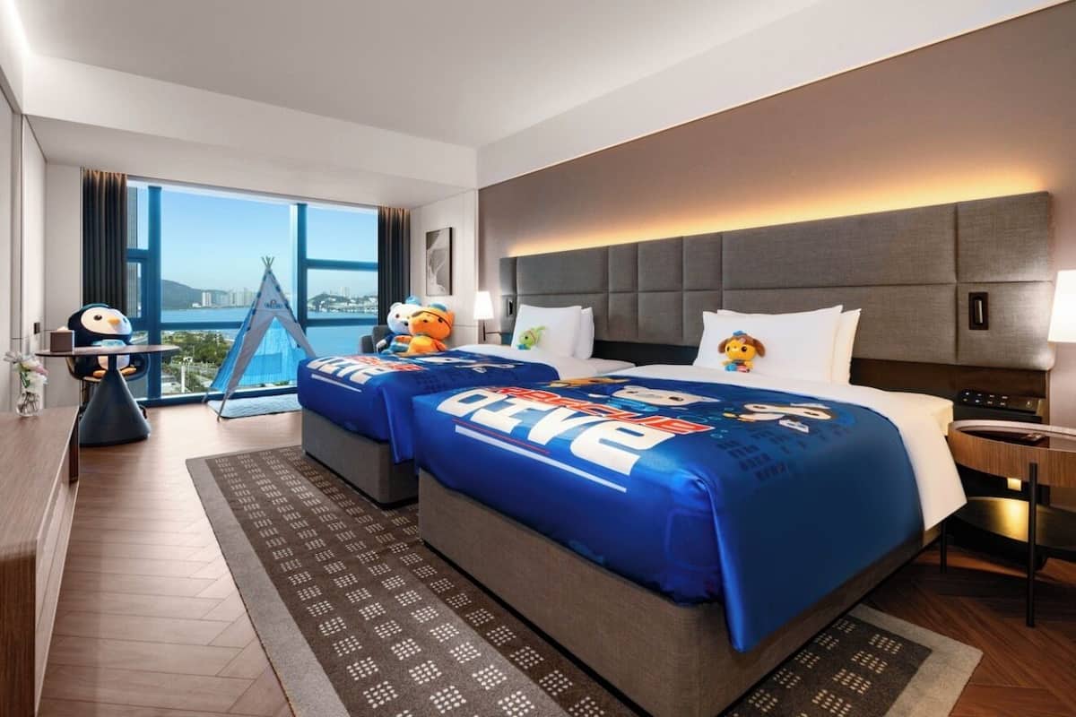 A hotel room with a large bed, a desk, a chair, and a view of the city.