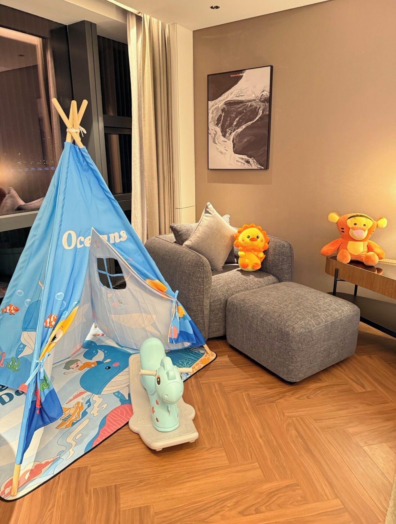Un salon chaleureux avec une tente bleue, des peluches et un canapé gris.