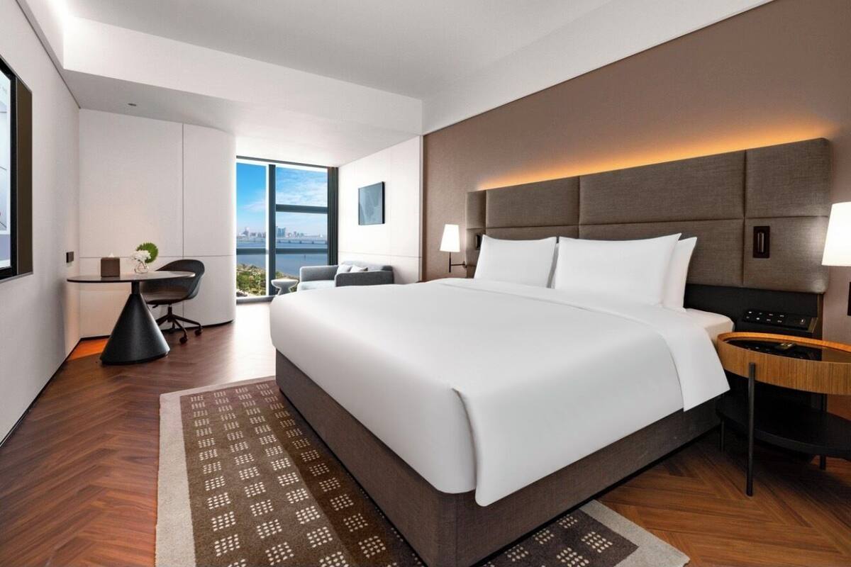 A modern hotel room with a large bed, a desk, and a view of the city.