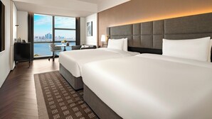 Habitación de hotel con dos camas, un escritorio, una silla y vistas del horizonte de la ciudad.