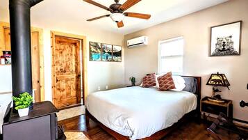 Un dormitorio con cama, ventilador de techo, calefactor, ventana y puerta.
