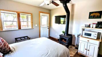 Un dormitorio con cama, ventilador de techo, chimenea, televisor y microondas.