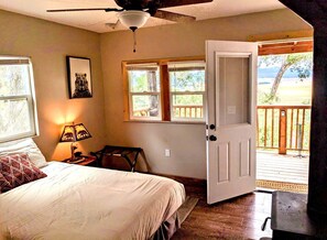 A bedroom with a bed, a desk, a chair, a window, and a door leading to a balcony. - Santa Ysabel Lakeview Glamping: Your Secluded Nature Escape (Santa Ysabel)