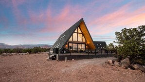 Un edificio moderno dalla forma triangolare, con ampie finestre e un balcone, immerso in un paesaggio desertico con montagne sullo sfondo.
