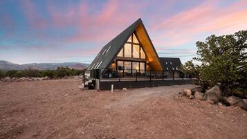 A modern, triangular-shaped building with large windows and a balcony, set in a desert landscape with mountains in the background.