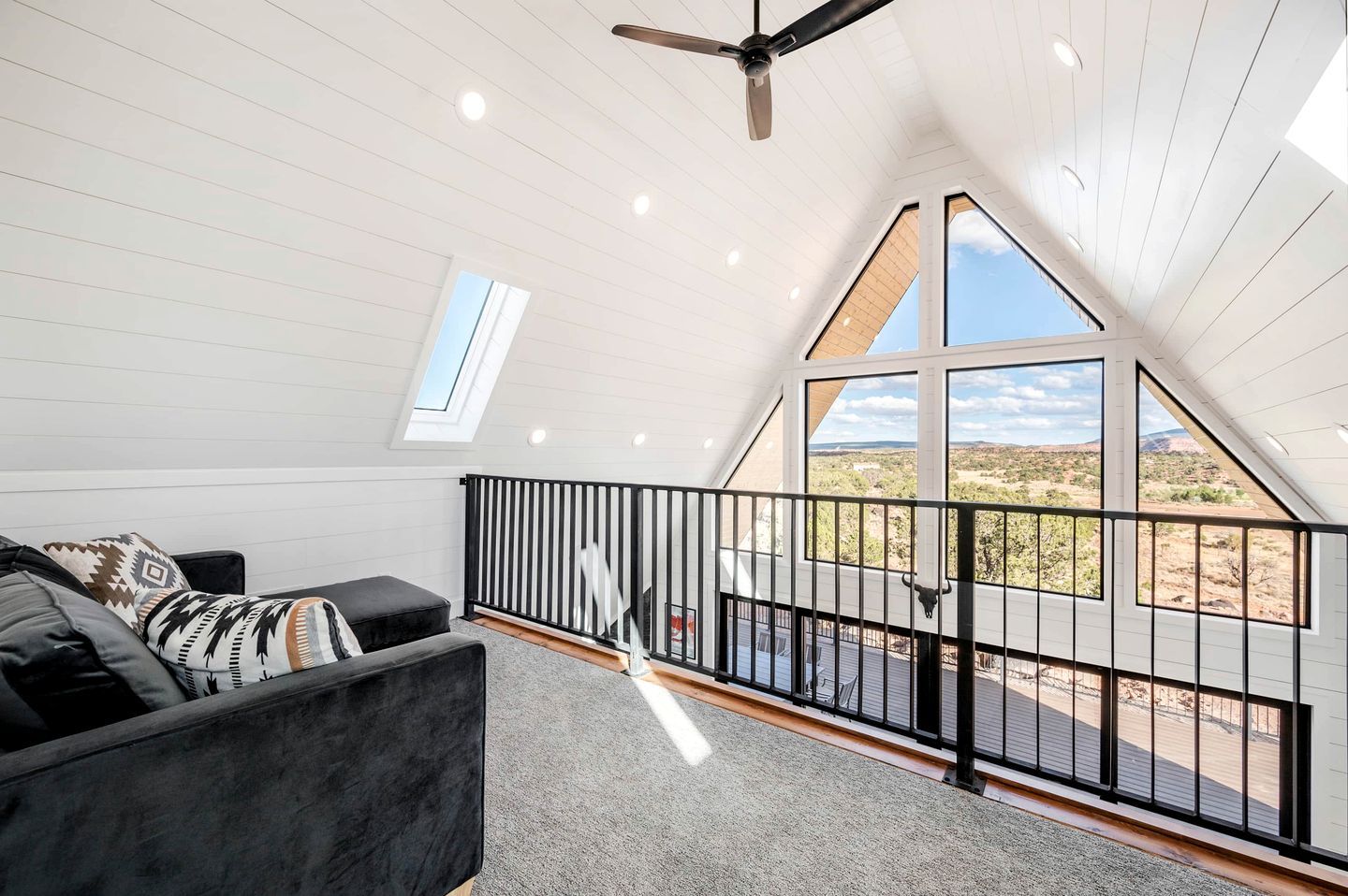 A modern loft bedroom with a large skylight, a ceiling fan, and a view of a desert landscape.