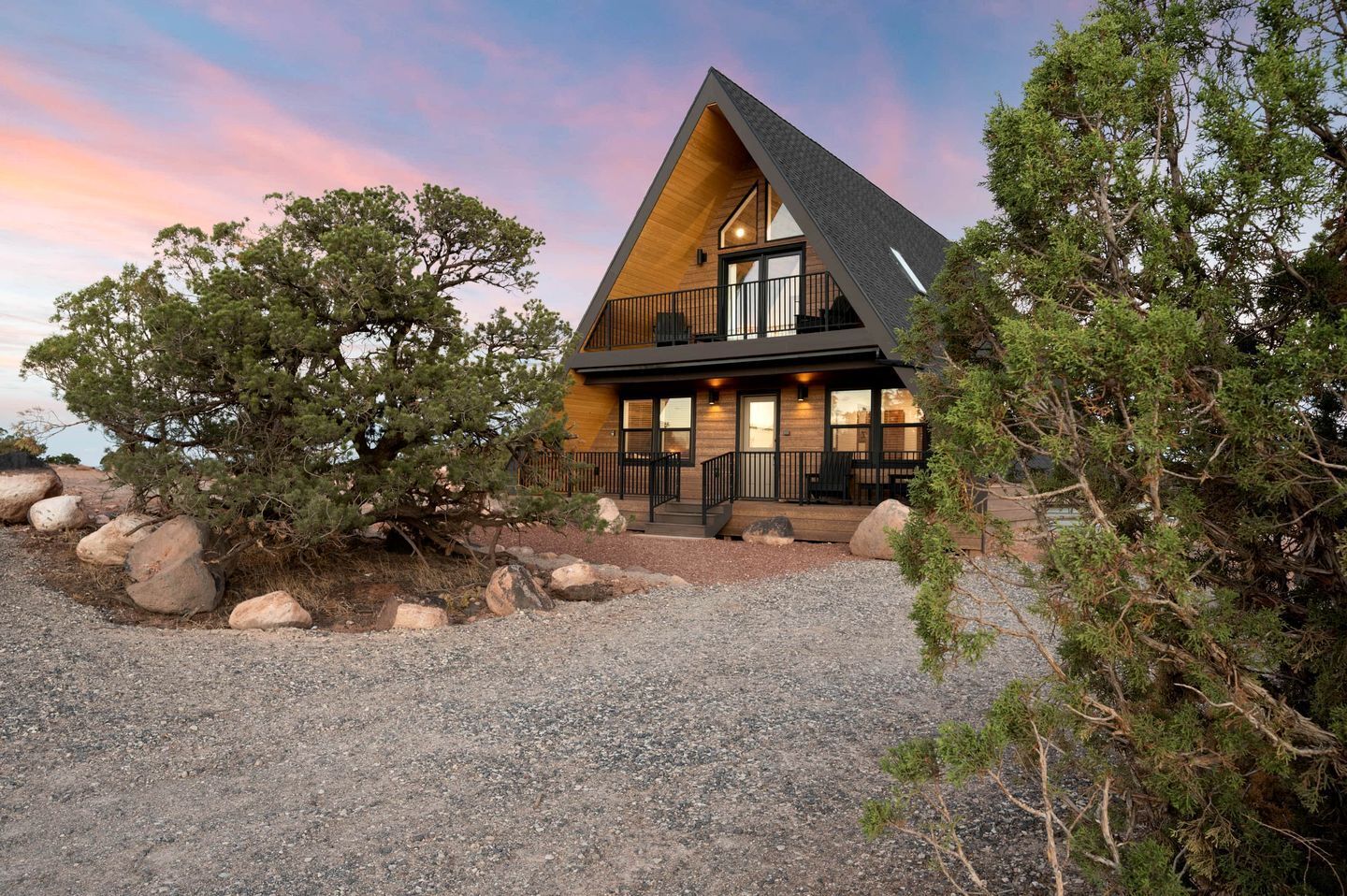 A modern house with a triangular roof, large windows, and a gravel driveway.