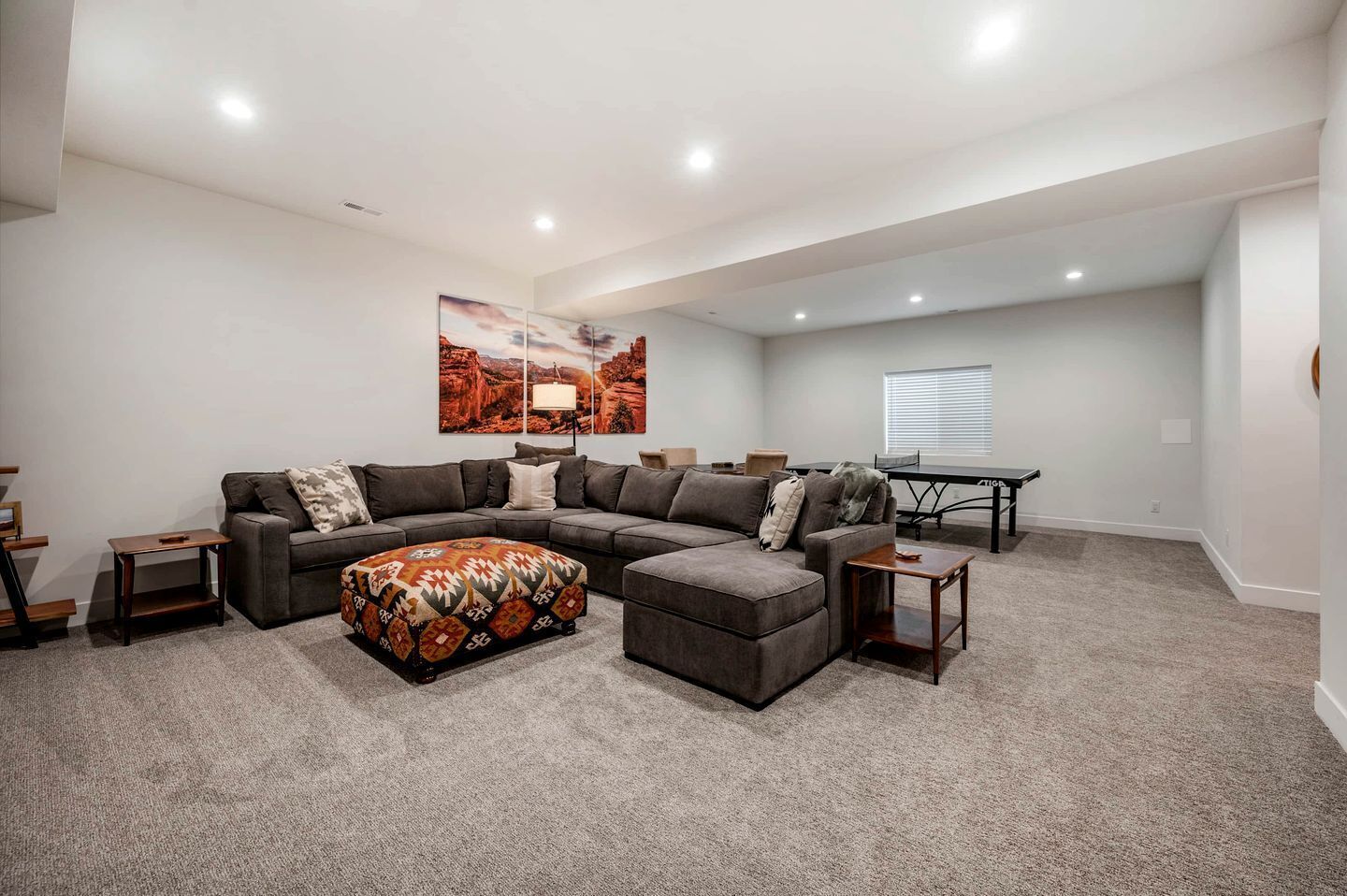 A living room with a sectional sofa, ottoman, and a painting on the wall.