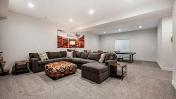 A living room with a sectional sofa, ottoman, and a painting on the wall.
