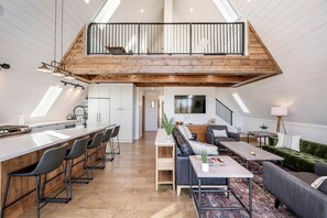 Ein geräumiges Loft mit hohen Decken, einer Küche mit Bar, einem Wohnzimmer mit Sofa und Couchtisch sowie einer Treppe zu einer oberen Ebene.