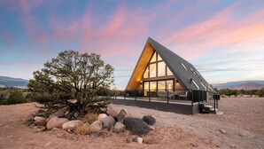 A modern, triangular building with large windows, a patio area, and a view of the surrounding landscape. - Experience Pure Glamping on this A-frame Placed in the Middle of the Desert in Wayne County, Utah (Wayne County)