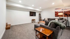 Un soggiorno moderno con un divano grigio, un tavolino in legno, una TV a parete e un quadro raffigurante un paesaggio desertico.