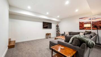 Ein modernes Wohnzimmer mit grauem Sofa, einem Holztisch, einem an der Wand befestigten Fernseher und einem Gemälde einer Wüstenlandschaft.