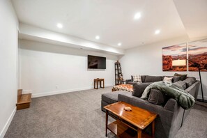 A modern living room with a grey sofa, a wooden coffee table, a TV mounted on the wall, and a painting of a desert landscape. - Experience Pure Glamping on this A-frame Placed in the Middle of the Desert in Wayne County, Utah (Wayne County)