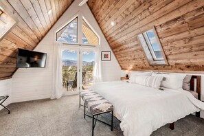 A bedroom with a large bed, a TV, a bench, and a balcony with a view. - Experience Pure Glamping on this A-frame Placed in the Middle of the Desert in Wayne County, Utah (Wayne County)