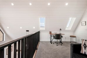A loft bedroom with a desk, chair, and a view of the sky through skylights.