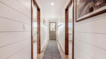 A hallway with white paneling, wooden doors, a gray carpet, and a framed picture on the wall.