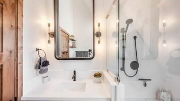 A modern bathroom with a white sink, a large mirror, a glass-enclosed shower, and wooden cabinetry.