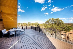 A wooden deck with a table and chairs, a metal railing, and a view of trees and hills. - Experience Pure Glamping on this A-frame Placed in the Middle of the Desert in Wayne County, Utah (Wayne County)