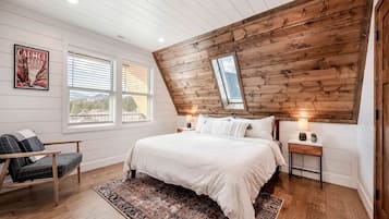 A bedroom with a sloped ceiling, a large bed, a chair, a nightstand, a lamp, and a poster on the wall.