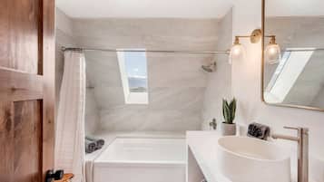 A modern bathroom with a bathtub, a large mirror, a sink, and a shower.