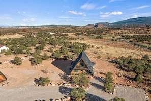 A remote, triangular-shaped cabin surrounded by a dry, hilly landscape with sparse vegetation and distant mountains. - Experience Pure Glamping on this A-frame Placed in the Middle of the Desert in Wayne County, Utah (Wayne County)