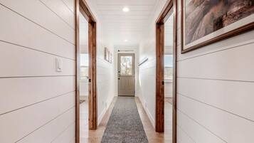 A hallway with white paneling, wooden doors, a gray carpet, and a framed picture on the wall.